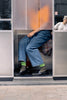 Person sitting inside a bus with a blurred face, wearing blue jeans and green socks.