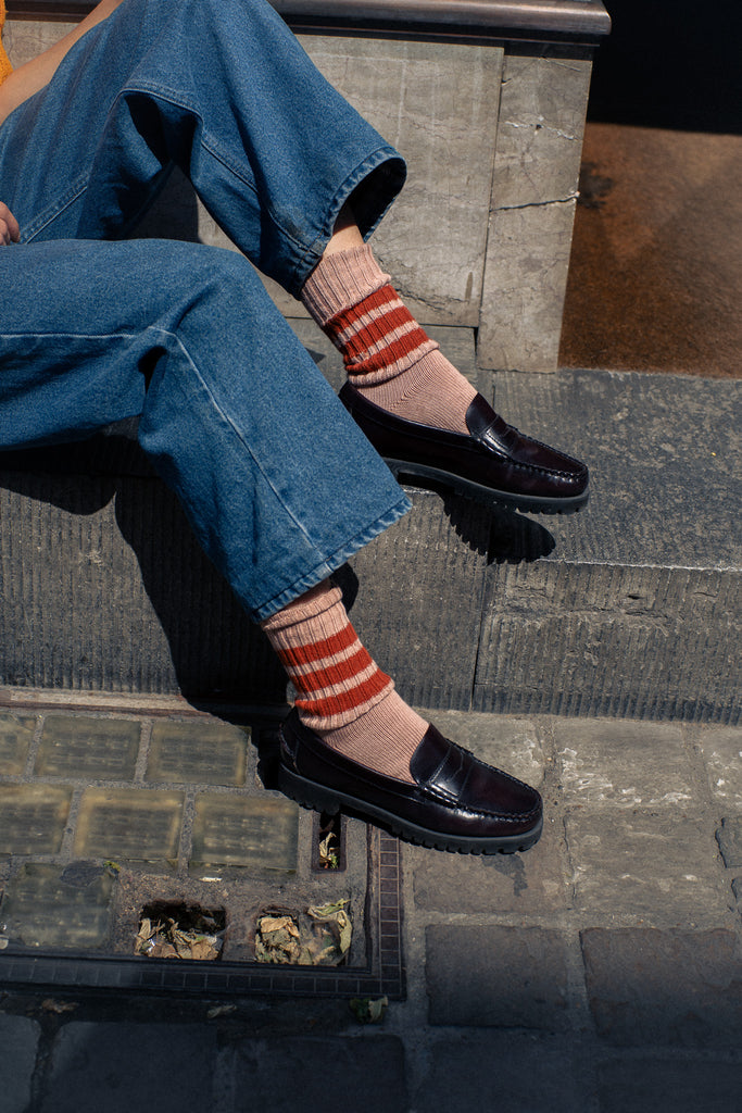 Person wearing blue jeans, black loafer shoes, and striped Escuyer socks sitting on a stone step.