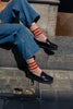 Person wearing blue jeans, black loafer shoes, and striped socks sitting on a stone step.