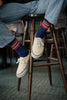 Person wearing blue jeans and white sneakers from Vans Skateboards with red and blue striped socks from Escuyer brand