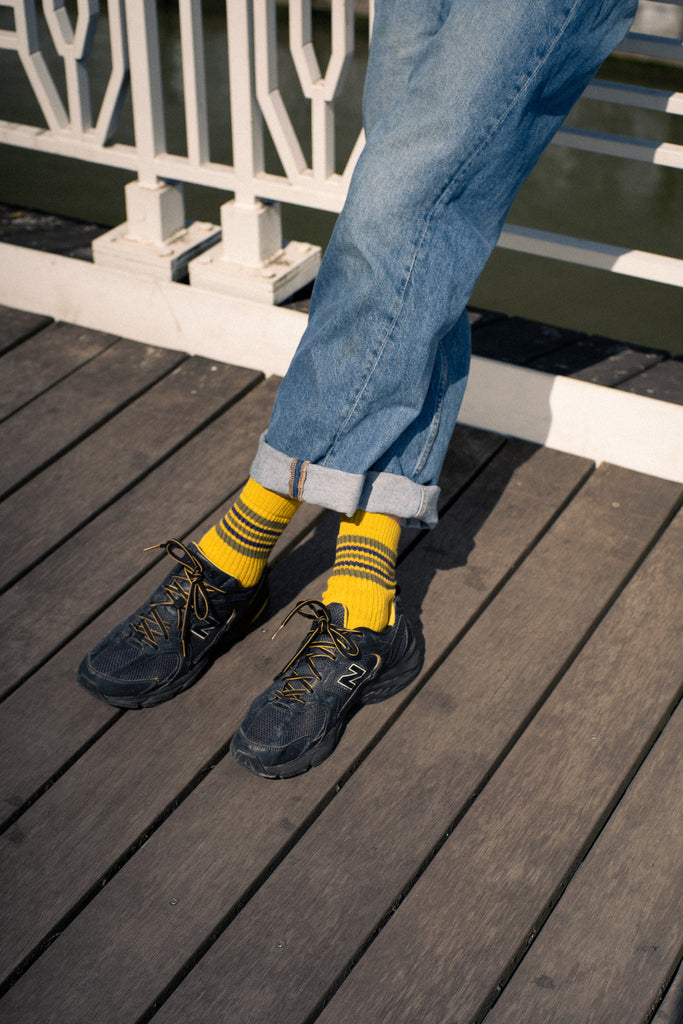Person wearing yellow striped socks with rolled-up jeans and dark shoes on a wooden deck.