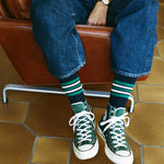 Person wearing green sneakers and blue jeans sitting on a brown leather chair with a tiled floor.