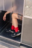 Person wearing red wool and cashmere socks from Escuyer and black sneakers from New Balance stepping out of a door.