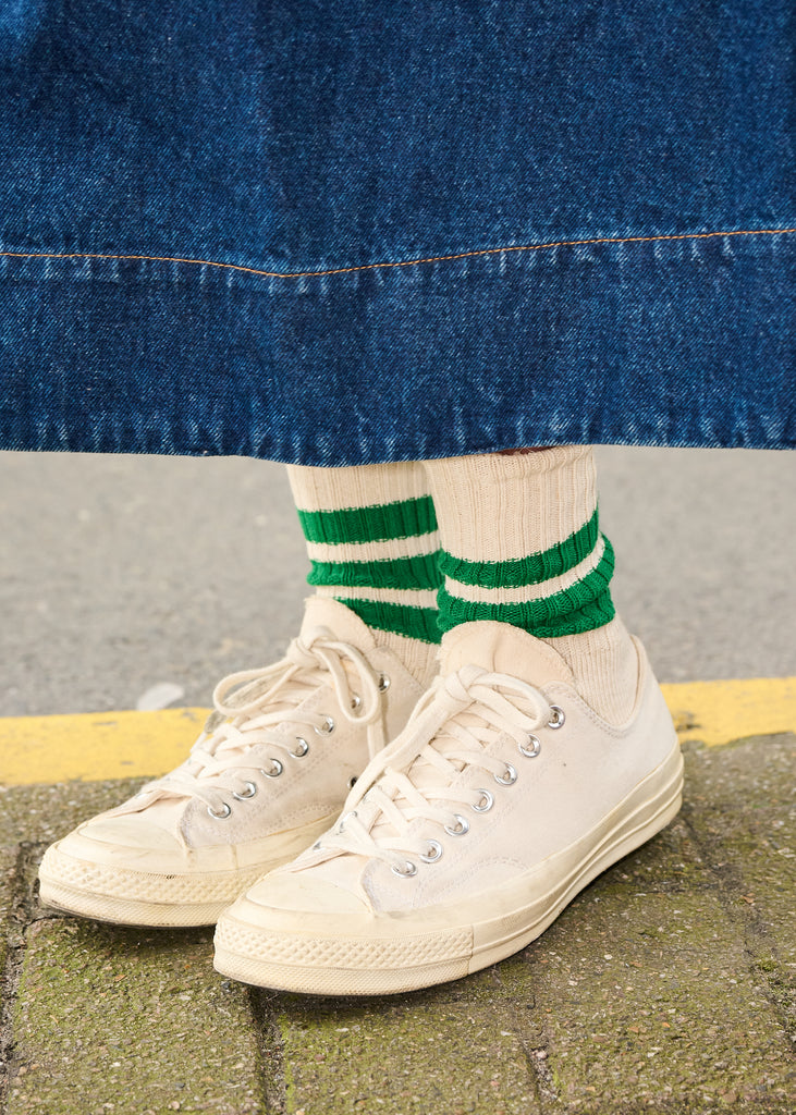 White sneakers with green striped socks worn under a blue denim skirt.