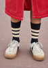 Person wearing red shorts, white sneakers, and black and beige striped socks on a neutral background