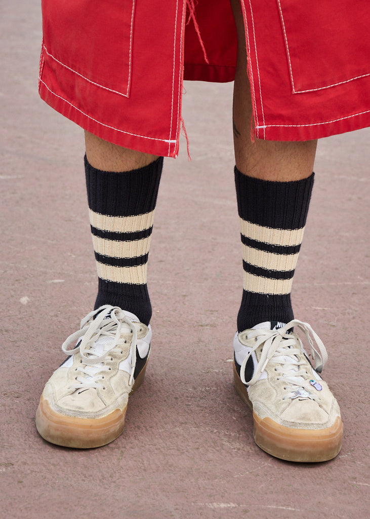 Person wearing red shorts, white sneakers, and black and beige striped socks on a neutral background