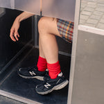 Person wearing red socks and black sneakers stepping out of a door.