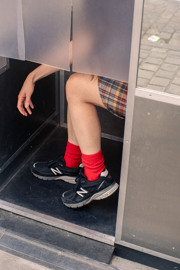 Person wearing red socks and black sneakers stepping out of a door.